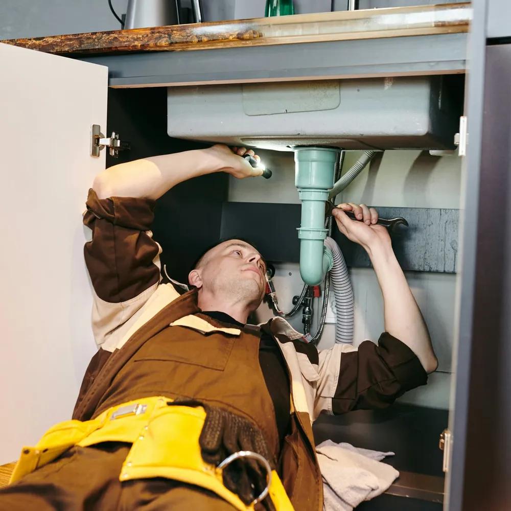 A plumber working under a sink, focused on the repair in front of him